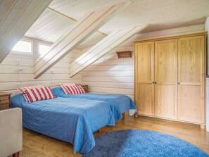 A bedroom with a sloped ceiling, two beds with blue bedding, a wooden wardrobe, and a blue rug.