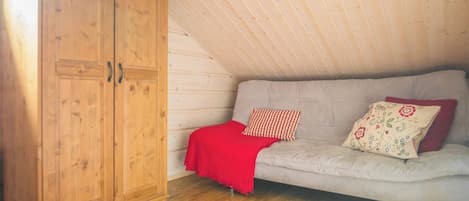 Ein Zimmer mit einem Holzschrank, einer grauen Couch mit floralen Kissen und einer roten Decke.