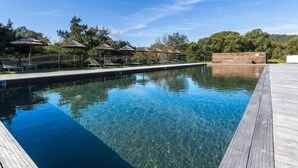 A clear swimming pool with wooden deck and lounge chairs, surrounded by trees and a wooden fence.
