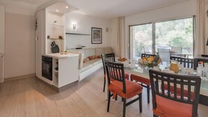 A modern kitchen with white cabinets, a built-in oven, and a dining area with a glass table and wooden chairs.