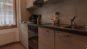 Una cuina moderna amb electrodomèstics d'acer inoxidable, armaris de fusta i una finestra amb cortines translúcides.