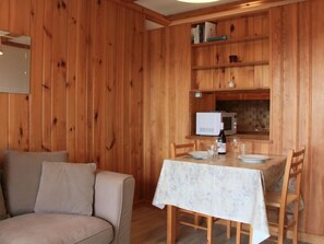 Une pièce chaleureuse avec des murs en bois, un canapé, une table à manger avec des chaises, un four à micro-ondes et une petite bibliothèque.