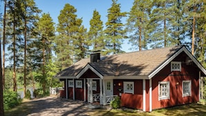 A red wooden cabin with a gravel driveway, surrounded by tall pine trees. - Kivitasku by Interhome (Somero)
