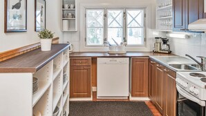 A modern kitchen with wooden cabinets, a dishwasher, a stove, and a sink. There are two windows with cross ventilation, a ceiling light, and a small plant on the counter. - Kivitasku by Interhome (Somero)
