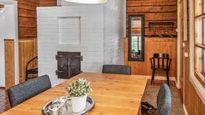 A wooden interior with a dining table, chairs, a hanging light fixture, a fireplace, and a mirror on the wall. - Kivitasku by Interhome (Somero)