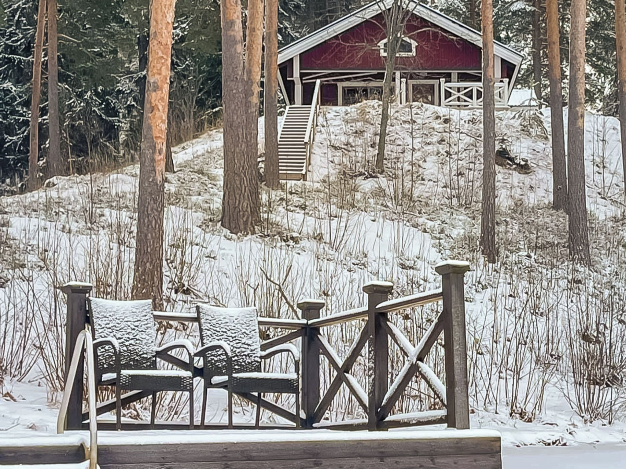 Um deck de madeira com guarda-corpo de metal, um celeiro vermelho ao fundo e uma paisagem nevada com árvores.