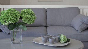 A living room with a grey sofa, a clear vase with green hydrangeas, and a tray with grey mugs.