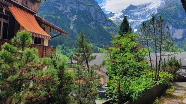 Un chalet de montagne avec une façade en bois, un auvent rouge et une vue sur des montagnes enneigées.