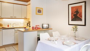 Une cuisine moderne avec des meubles blancs, un coin repas doté d’une table blanche pour quatre personnes et une œuvre d’art encadrée accrochée au mur.
