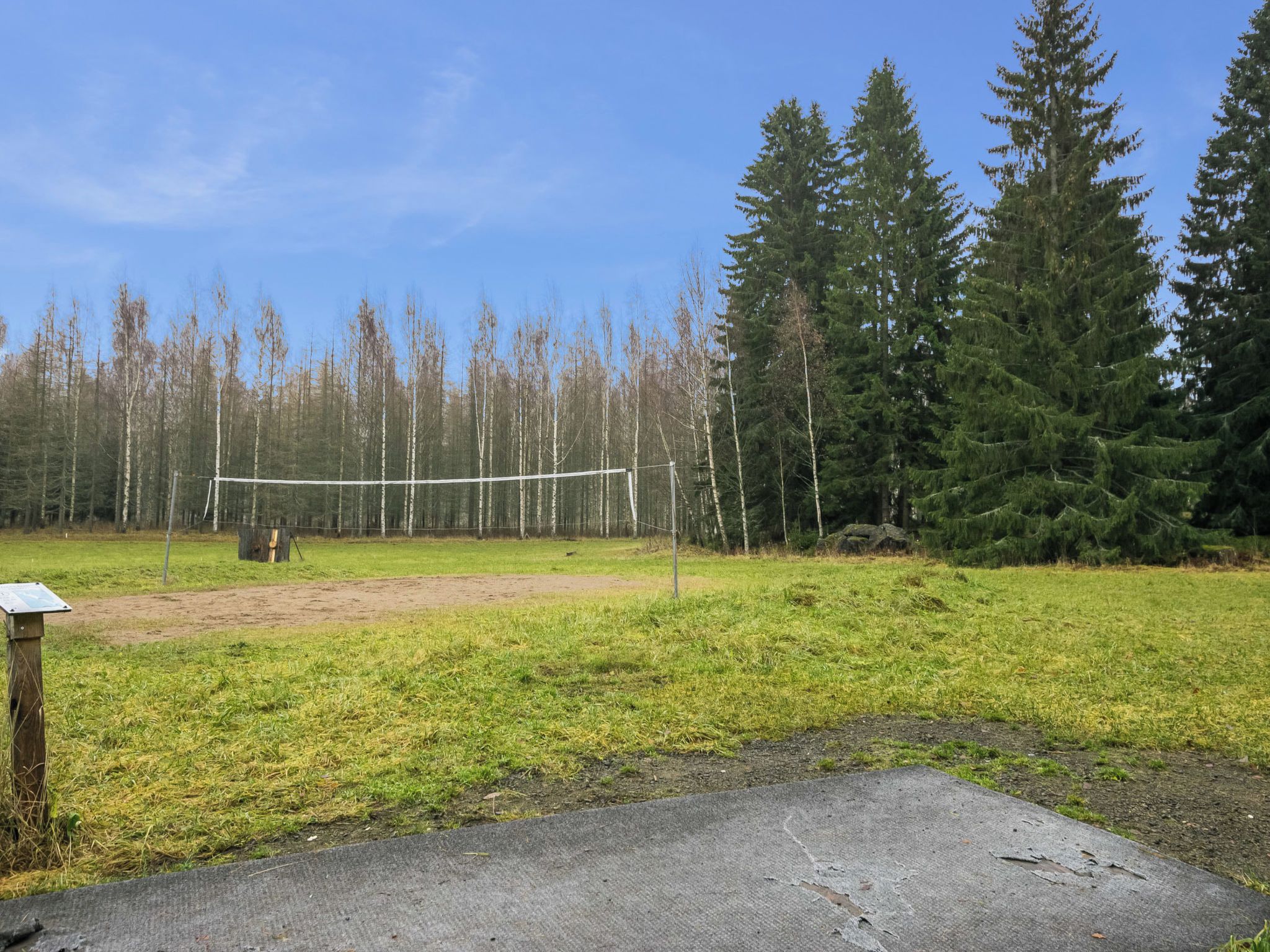 A volleyball court with a net, surrounded by a grassy field and trees.