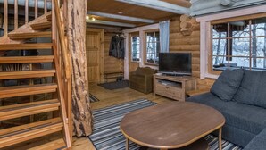 Interior de uma cabana de tronco com escada de madeira, televisão, sofá e uma janela grande.