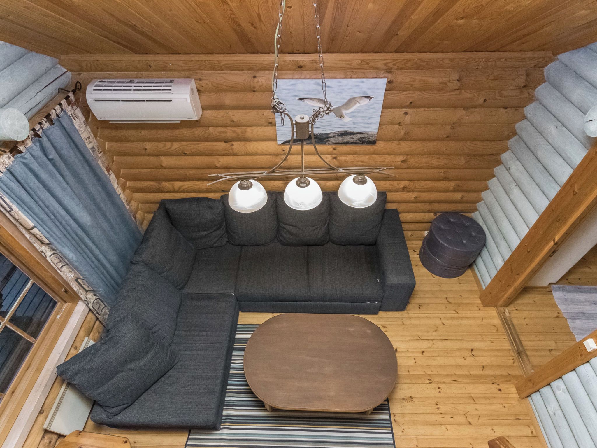 Interior acogedor de una cabaña con un sofá modular, un otoman redondo, una lámpara colgante y un cuadro con una imagen de un alce.