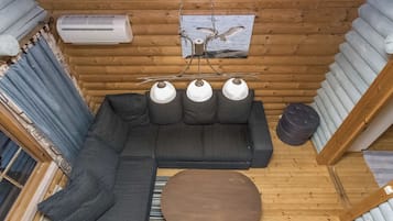 Interior acogedor de una cabaña con un sofá modular, un otoman redondo, una lámpara colgante y un cuadro con una imagen de un alce.