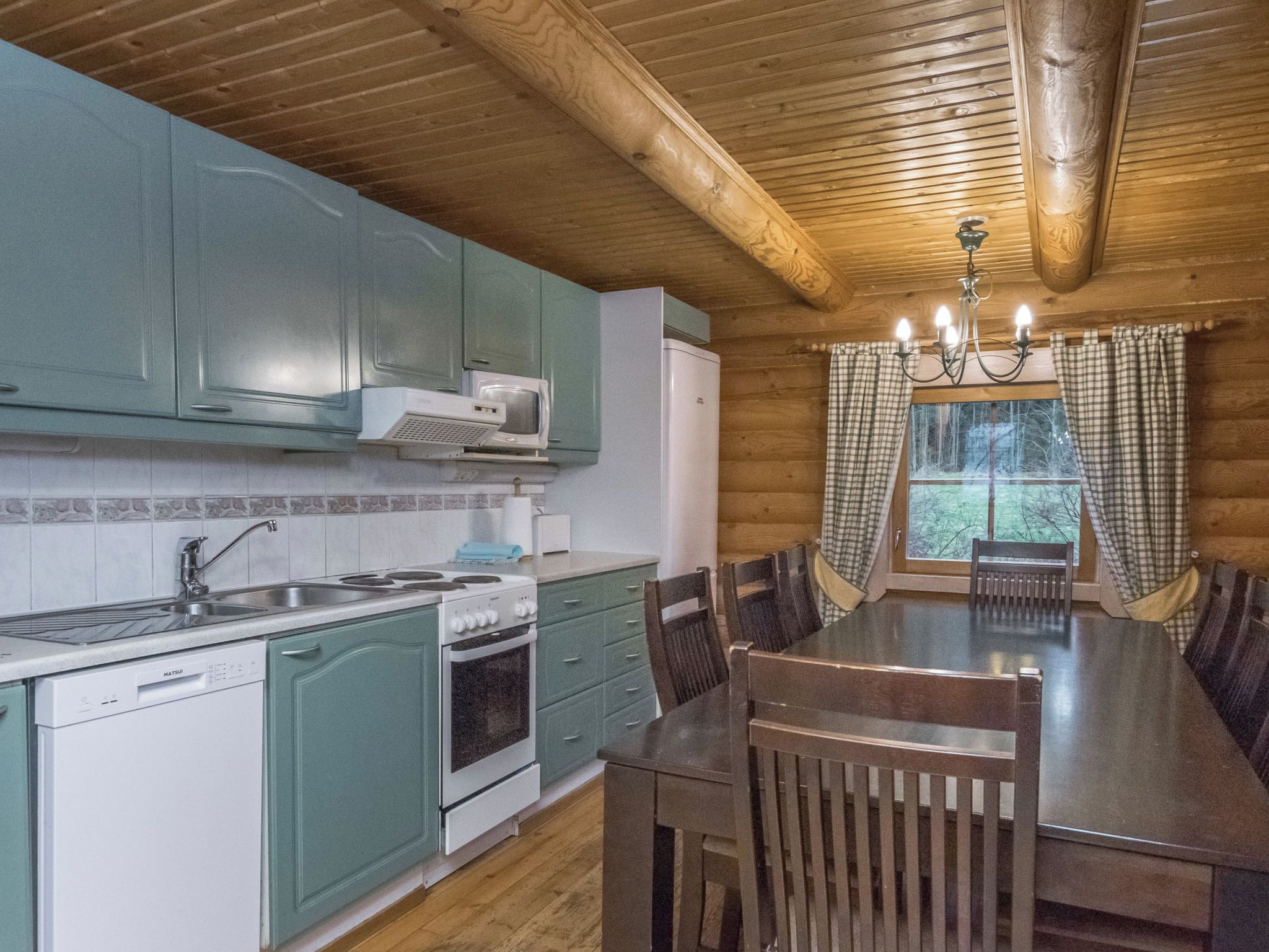 Une cuisine avec des meubles de rangement en bois, une cuisinière, un évier et une table à manger avec des chaises.