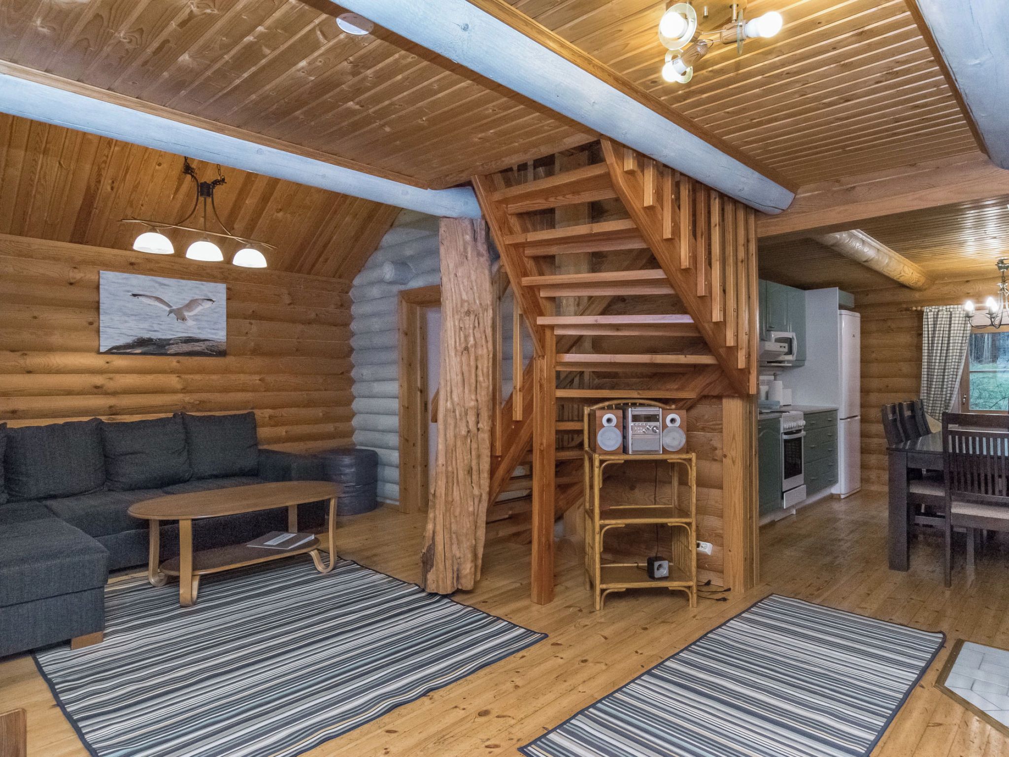 Ein rustikales Blockhaus-Interieur mit einer Holztreppe, einer Couch, einem Tisch und einer Küchenzeile.