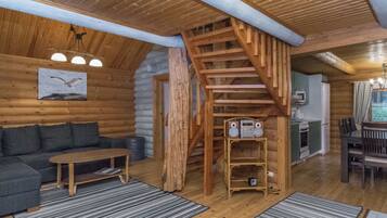 Ein rustikales Blockhaus-Interieur mit einer Holztreppe, einer Couch, einem Tisch und einer Küchenzeile.