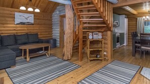 Interior de uma cabana de madeira com escada, sofá, mesa de jantar e área de cozinha.