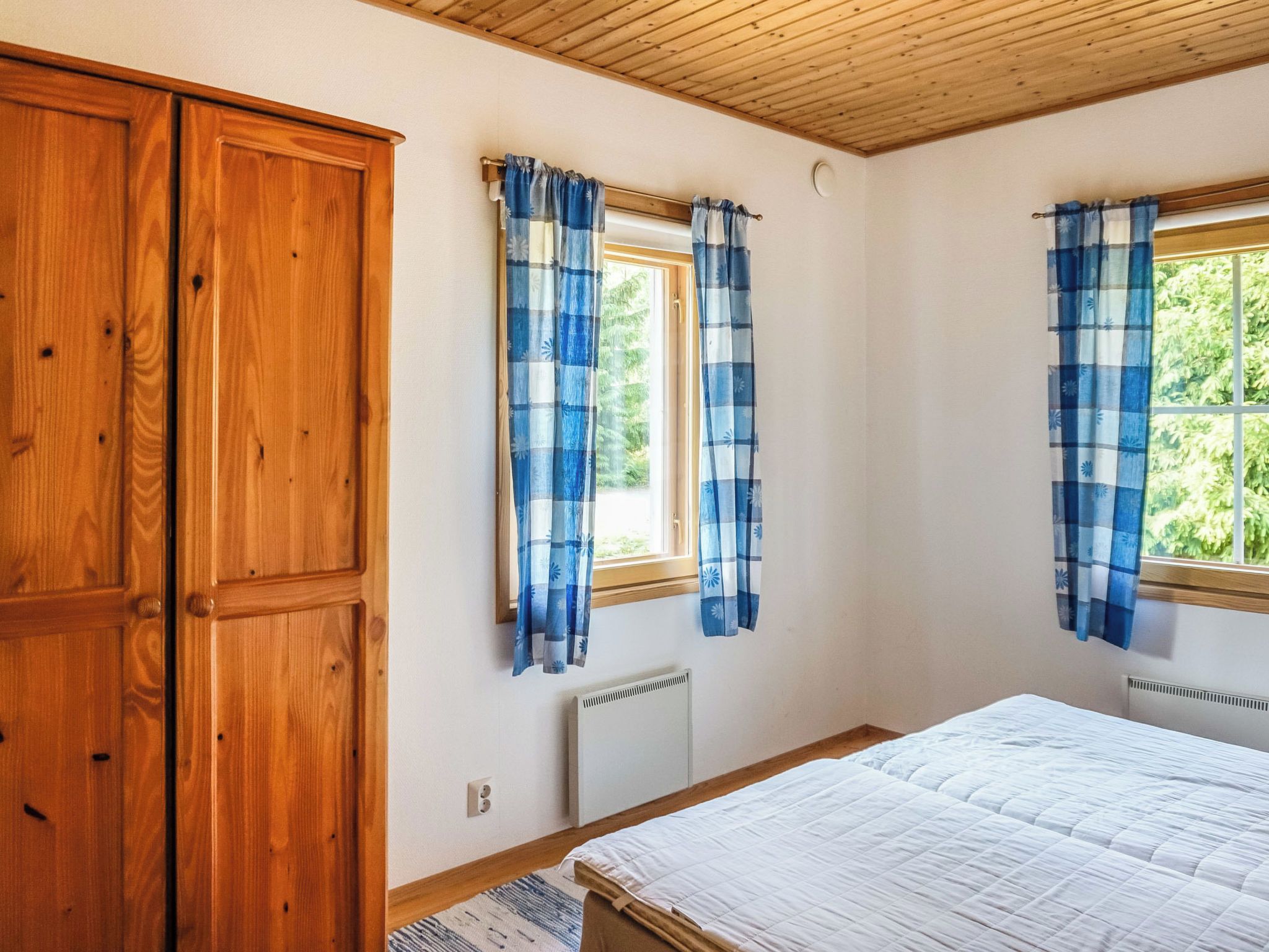 Makuuhuoneessa on puinen vaatekaappi, kaksi ikkunaa, joissa on siniset verhot, patteri ja sänky.