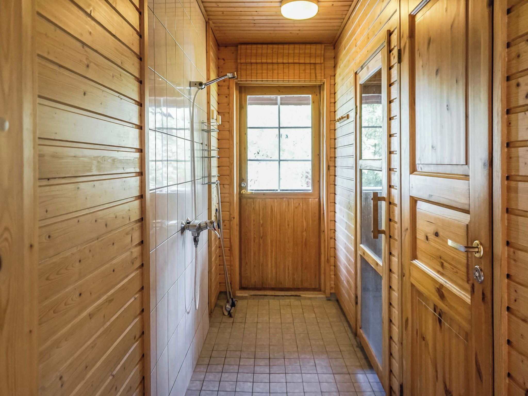 A narrow hallway with wooden walls and a tiled floor, leading to a door with a window.