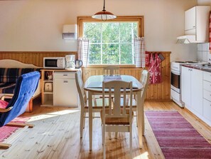 A compact kitchen with a dining table, chairs, a microwave, a coffee maker, and a window with a view of trees. - Naurulokki 4 by Interhome (Parainen)