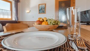 A dining area with a wooden table set for two, a bowl of fruit, and a television in the background. - Voithofer by Interhome (Königsleiten)