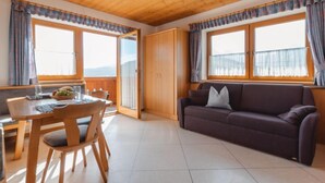 A room with a wooden ceiling, a dining table with chairs, a sofa, and large windows with curtains. - Voithofer by Interhome (Königsleiten)