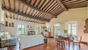 Un espacio habitable amplio con techo alto de madera, un sofá, una mesa de comedor con sillas y una cocina al fondo.