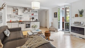 Una cuina moderna amb armaris blancs, una zona de menjador amb un sofà de pell marró i un televisor gran.