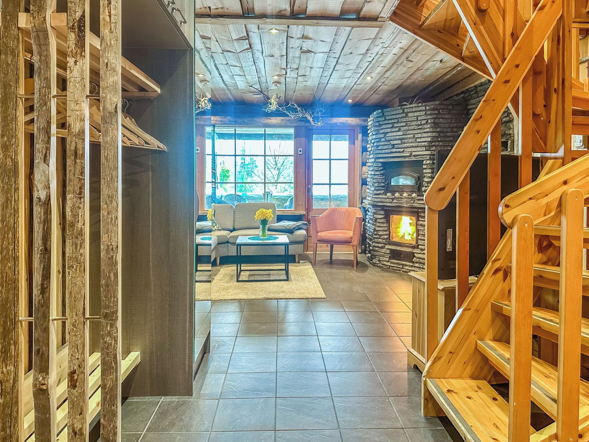 Un intérieur chaleureux avec une cheminée en pierre, un escalier en bois et un coin salon offrant une vue sur l’extérieur.
