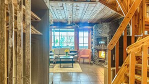 A cozy interior with a stone fireplace, wooden staircase, and a seating area with a view of the outdoors.