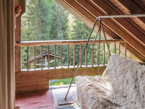 A wooden deck with a swing chair and a view of a forested area.