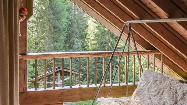 A cozy room with a wooden balcony, a fluffy white sofa, and a view of a forested area.
