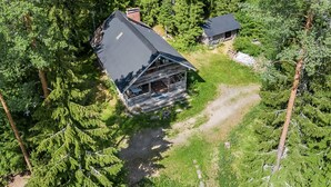 A cabin surrounded by dense forest, with a visible porch and a chimney.