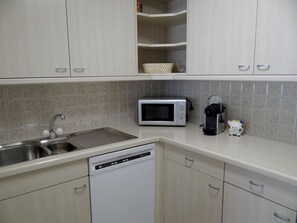 A kitchen with a dishwasher, a microwave, a kettle, and a sink.