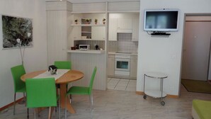 Un espacio habitable compacto con comedor, kitchenette y televisor montado en la pared.