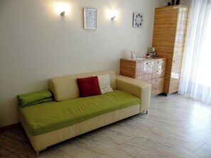 A modern living room with a beige sofa, a wooden cabinet, and a light-colored tiled floor.