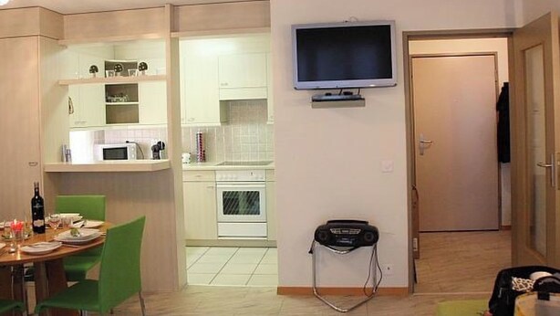 Un espacio habitable compacto con kitchenette, comedor y televisor montado en la pared.