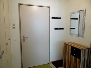 A closed door with a handle, a wall-mounted mirror with a decorative frame, and a small wooden cabinet with drawers.