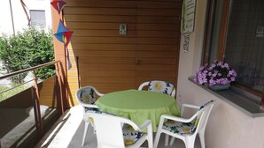 Un pequeño patio al aire libre con una mesa redonda y cuatro sillas, una cerca de madera y una ventana con una maceta de flores.