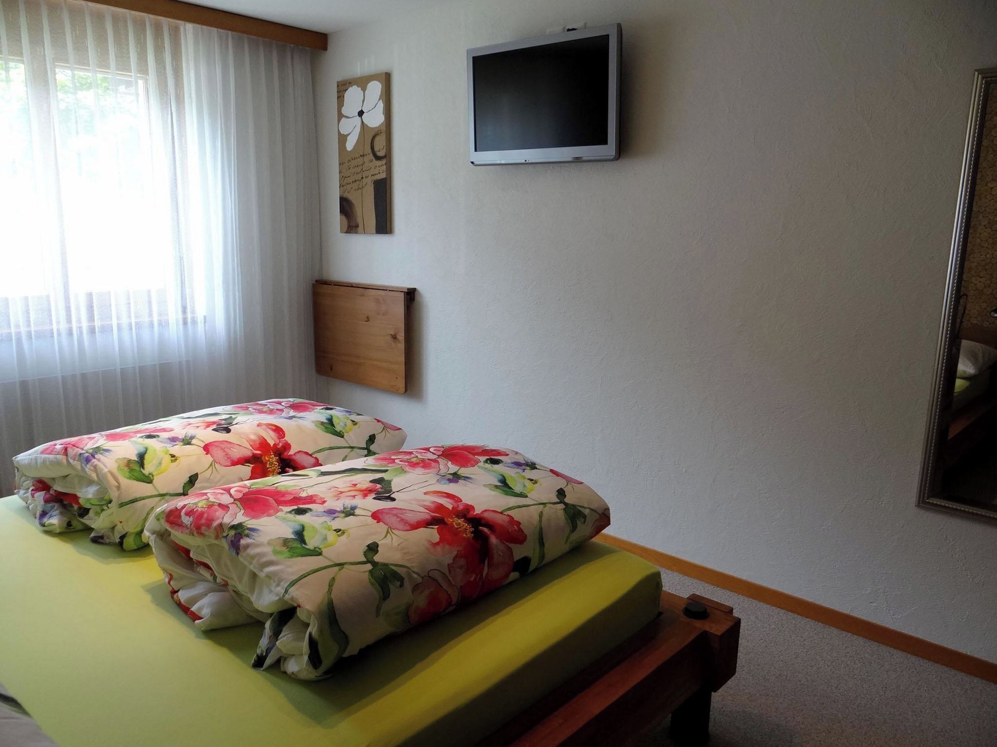 Una habitación con cama, televisión de pantalla plana, cabecero de madera y ventana con cortinas.