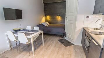A compact living space with a dining area, a bed, a kitchenette, and a TV mounted on the wall.
