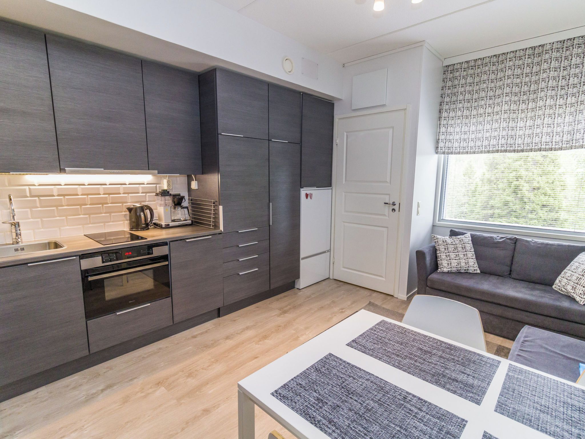 A modern kitchen with dark cabinetry, a built-in oven, and a coffee maker.