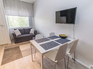 Uma sala de estar moderna com sofá, mesa de jantar com jogos americanos, televisão e janela com persianas.
