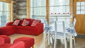 A log cabin interior with a red sofa, white chairs, and a dining table. - Kotkanpesä by Interhome (Kittilä)