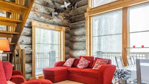 A cozy log cabin interior with a red sectional sofa, wooden dining table, and large windows. - Kotkanpesä by Interhome (Kittilä)