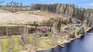 A house with a large deck, surrounded by a forest and a body of water.