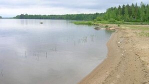 A calm lake with a sandy shore and dense forest in the background. - Taivaanranta by Interhome (Pyhäjärvi)