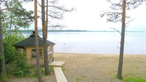 A wooden cabin with a deck, surrounded by trees, overlooking a calm lake. - Taivaanranta by Interhome (Pyhäjärvi)