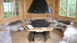 A room with a central wood-burning stove, wooden walls, and fur-covered benches. - Taivaanranta by Interhome (Pyhäjärvi)