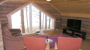 A cozy cabin interior with a large window, a round table, two chairs, a sofa, and a TV. - Taivaanranta by Interhome (Pyhäjärvi)
